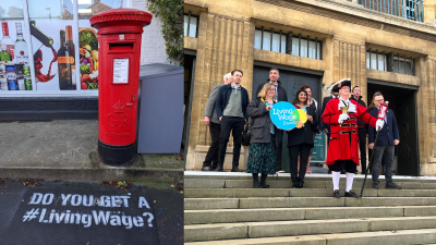 Red Royal Mail post box with 'Do you get a #LivingWage?' graffiti'd on the pavement in front of it. A town crier and a group of people standing on the steps of Norwich Town Hall