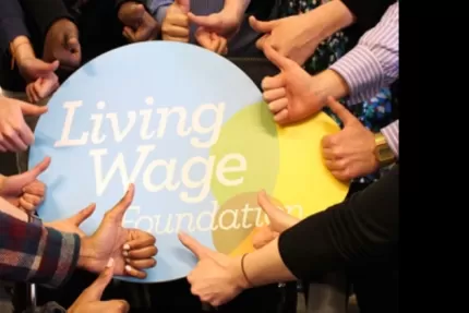 Living Wage Foundation foamboard surrounded by a circle of hands giving it the thumbs up