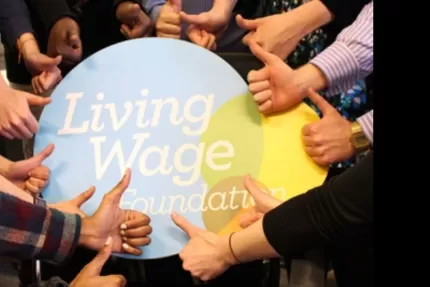Living Wage Foundation foamboard surrounded by a circle of hands giving it the thumbs up
