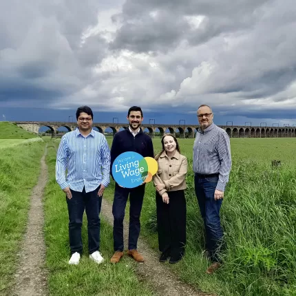 Capital Cleaning Staff stand in a field, holding a 'Living Wage Employer' sign