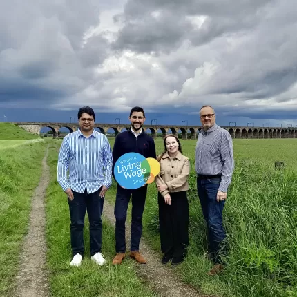 Capital CleaniCapital Cleaning Staff stand in a field, holding a 'Living Wage Employer' signng Staff stand in a field, holding a 'Living Wage Employer' sign