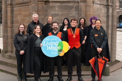 Mercat staff hold a blue sign that reads "Living Wage Employer"